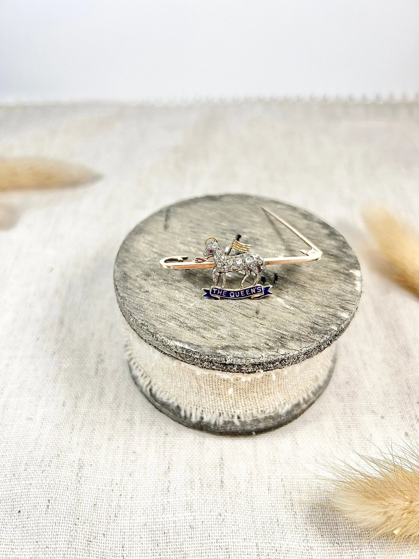 A diamond set regimental bar brooch in gold, with a blue enamel banner reading THE QUEEN'S