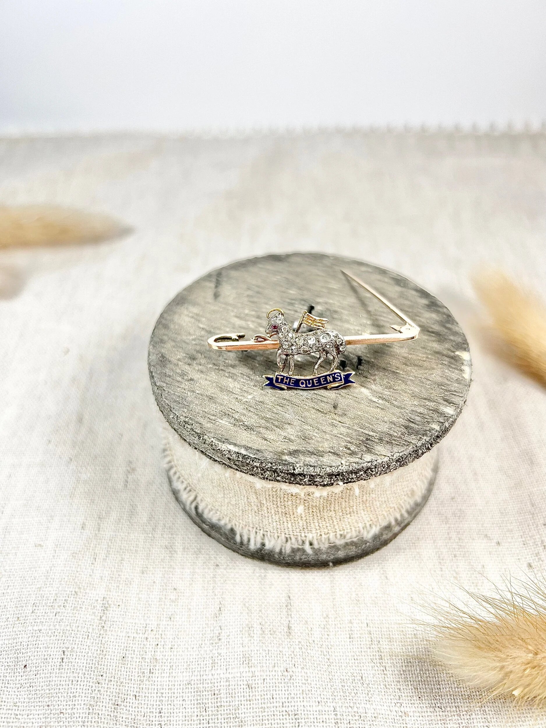 A diamond set regimental bar brooch in gold, with a blue enamel banner reading THE QUEEN'S