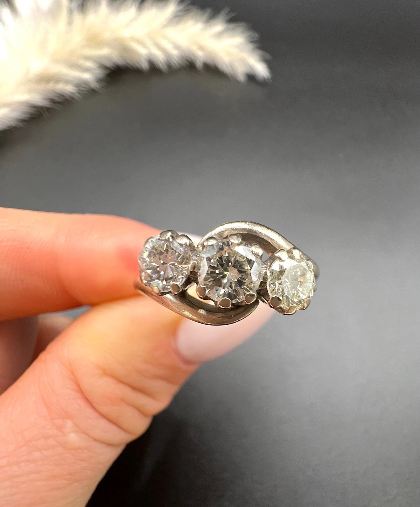 A three stone diamond crossover ring, held in a hand