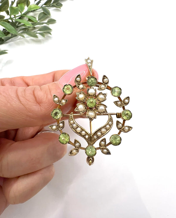 A peridot and pearl floral circle brooch/pendant in yellow gold, held in a hand