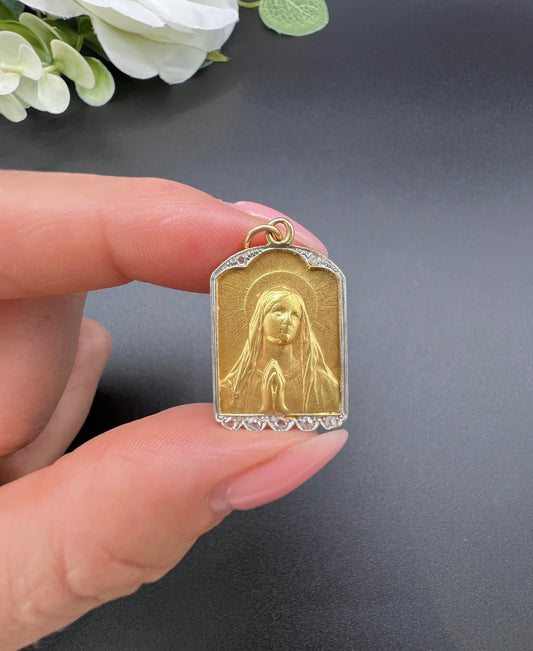 A yellow gold and platinum Madonna pendant with diamonds, held in a hand