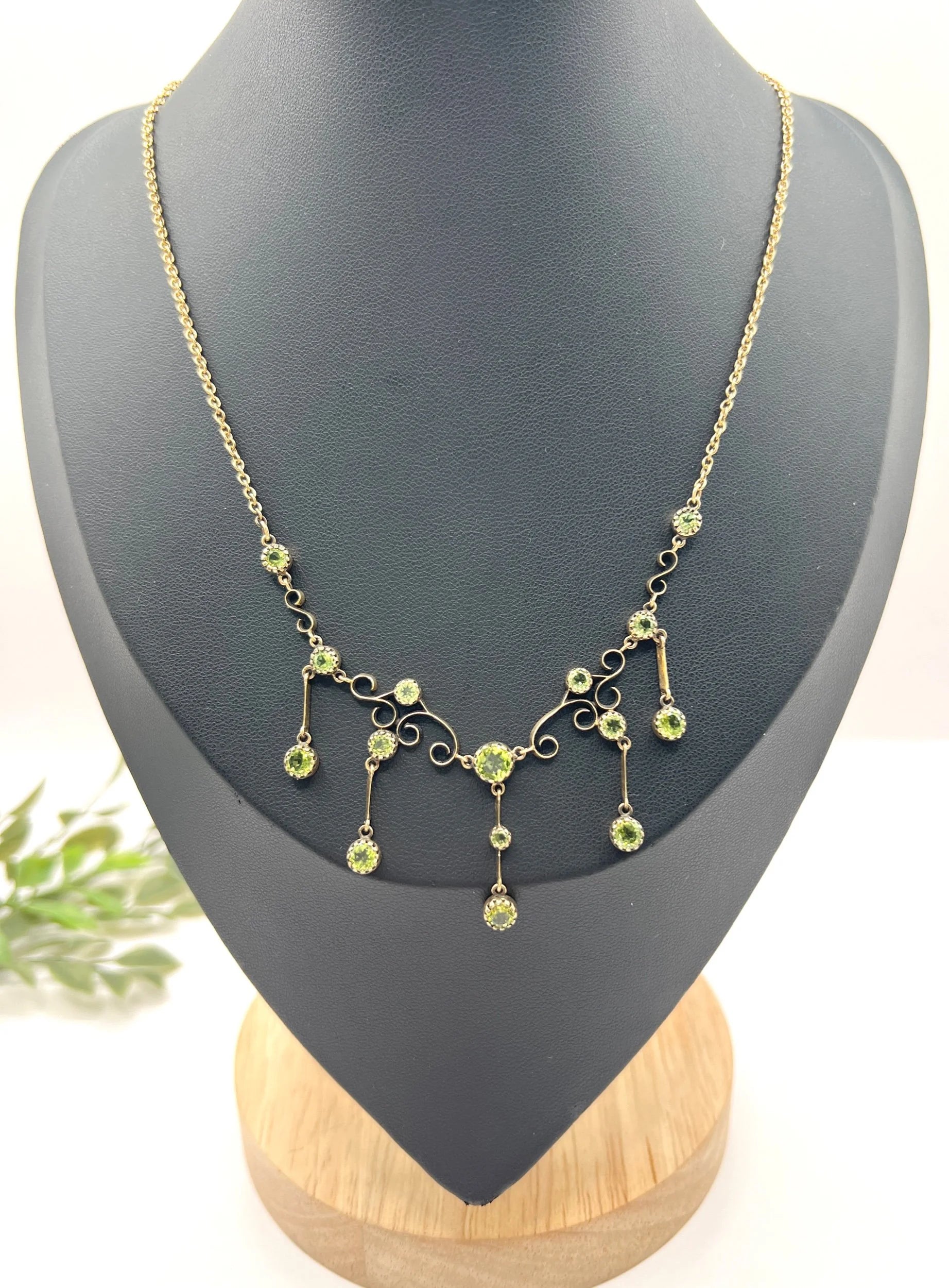A yellow gold swag necklace with peridot drops, on a black jewellery bust