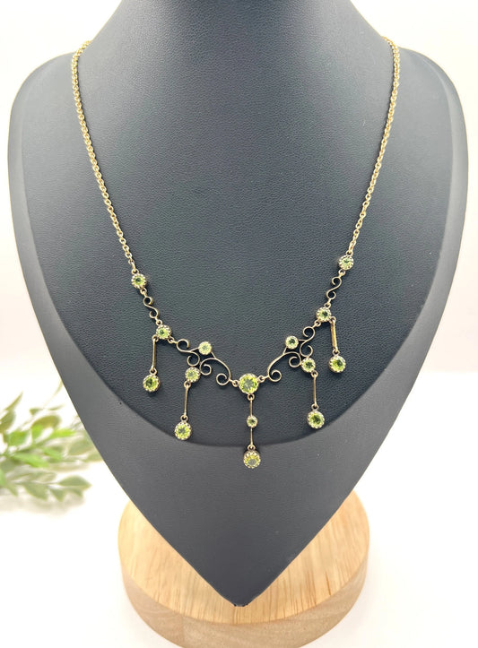 A yellow gold swag necklace with peridot drops, on a black jewellery bust