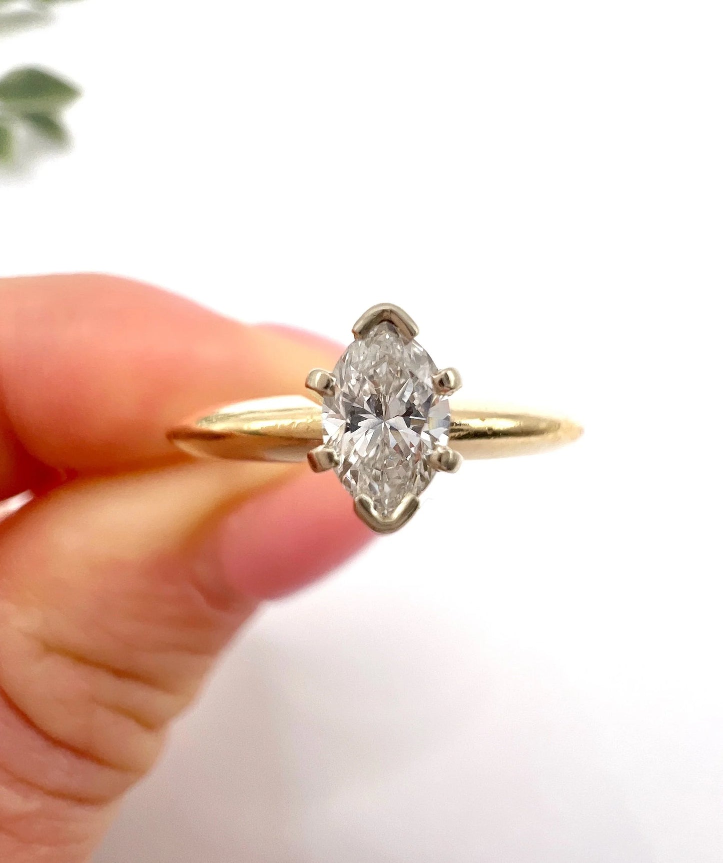 A marquise diamond solitaire ring in yellow and white gold, held in a hand