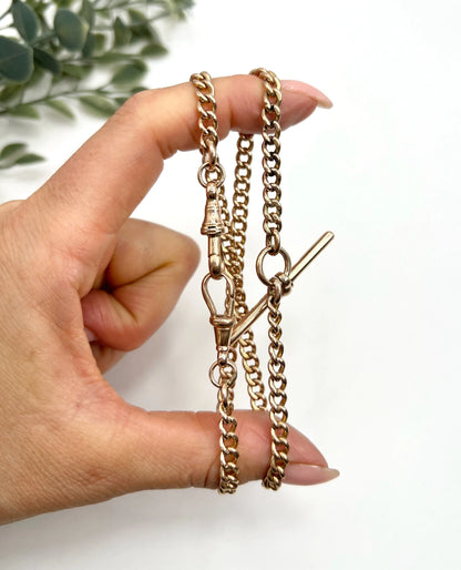 A gold curb link Albert chain, held in a hand