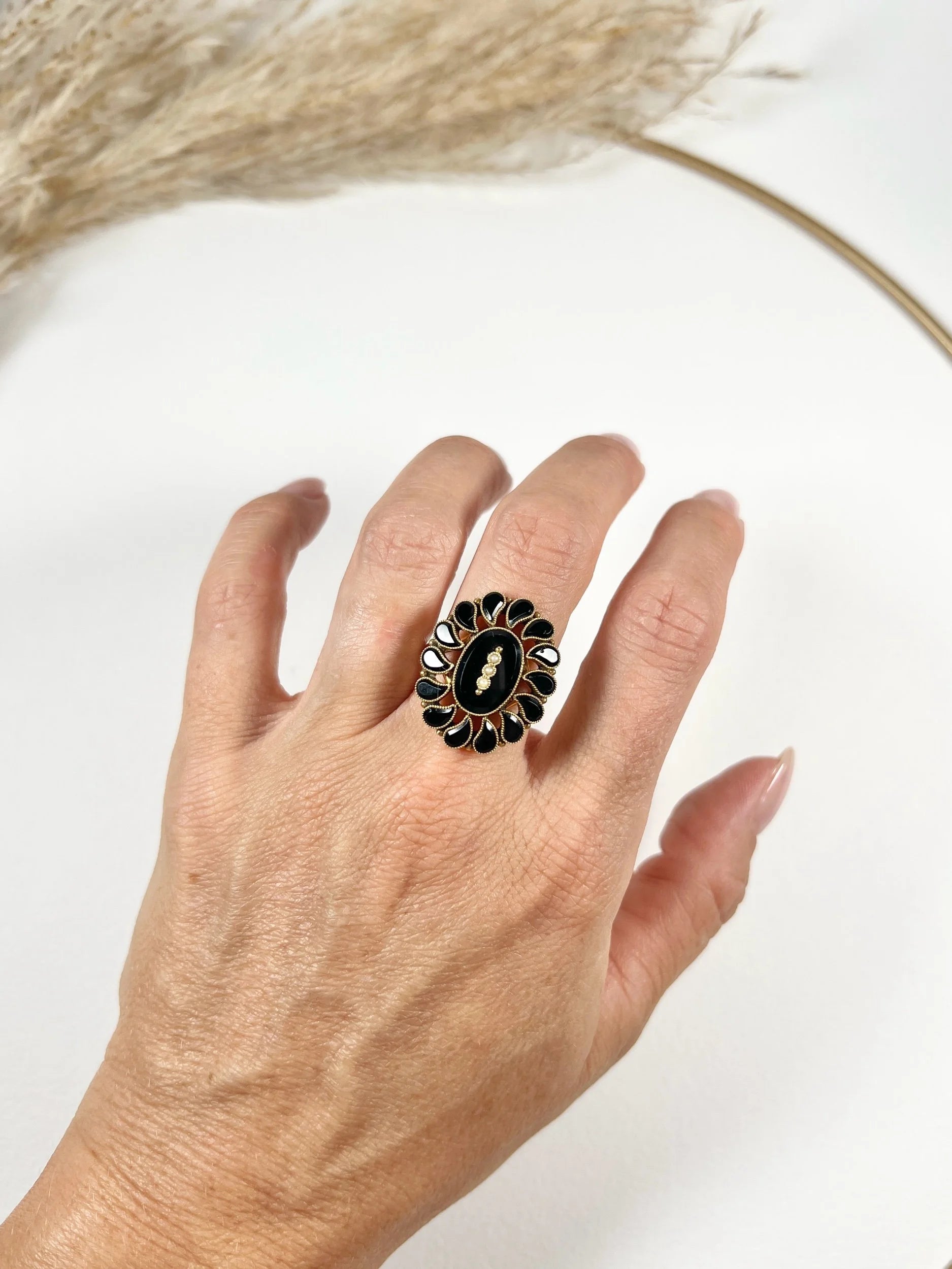 A black onyx and seed pearl fancy halo cluster ring in yellow gold, modelled on a hand