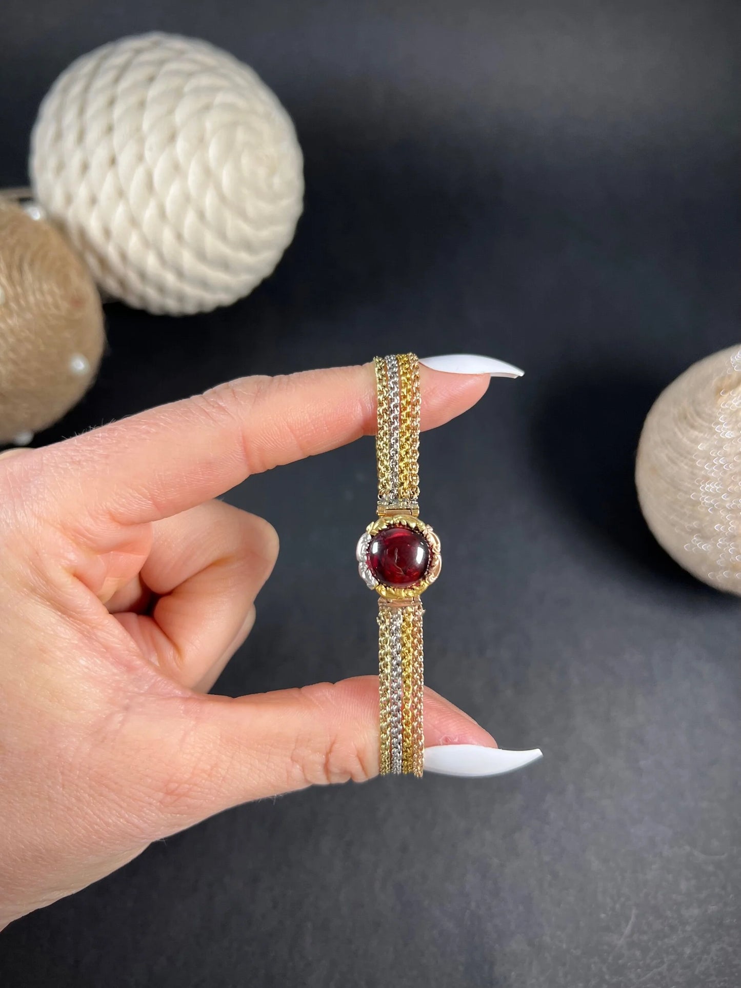 A cabochon garnet bracelet with three colour gold chains, held in a hand