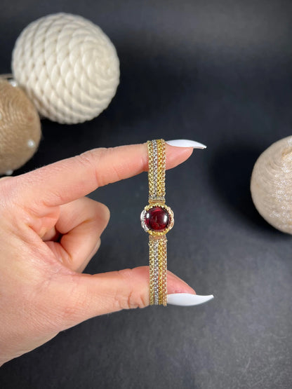 A cabochon garnet bracelet with three colour gold chains, held in a hand