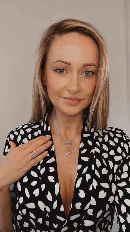 An antique diamond and pearl double drop pendant necklace, modelled by a woman wearing a black and white patterned top