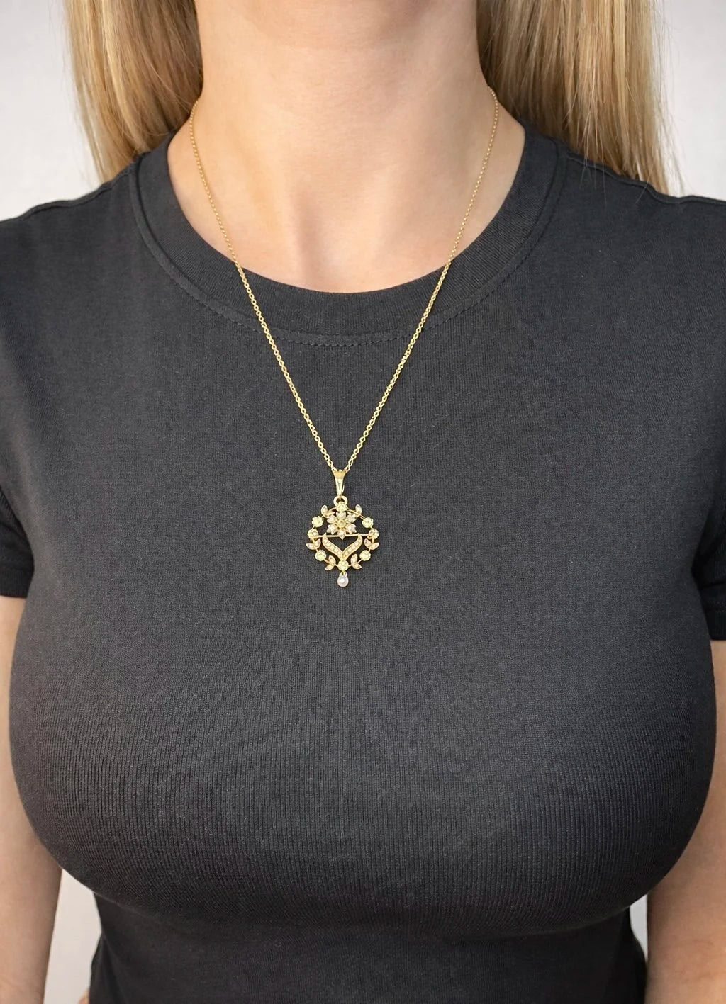 A peridot and pearl floral circle brooch/pendant in yellow gold, with a chain, modelled by a woman wearing a black top