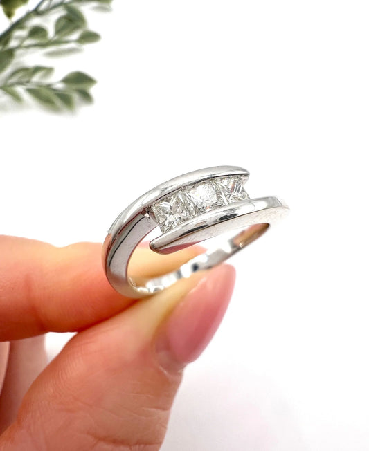 A three stone princess cut diamond crossover ring in white gold, held in a hand