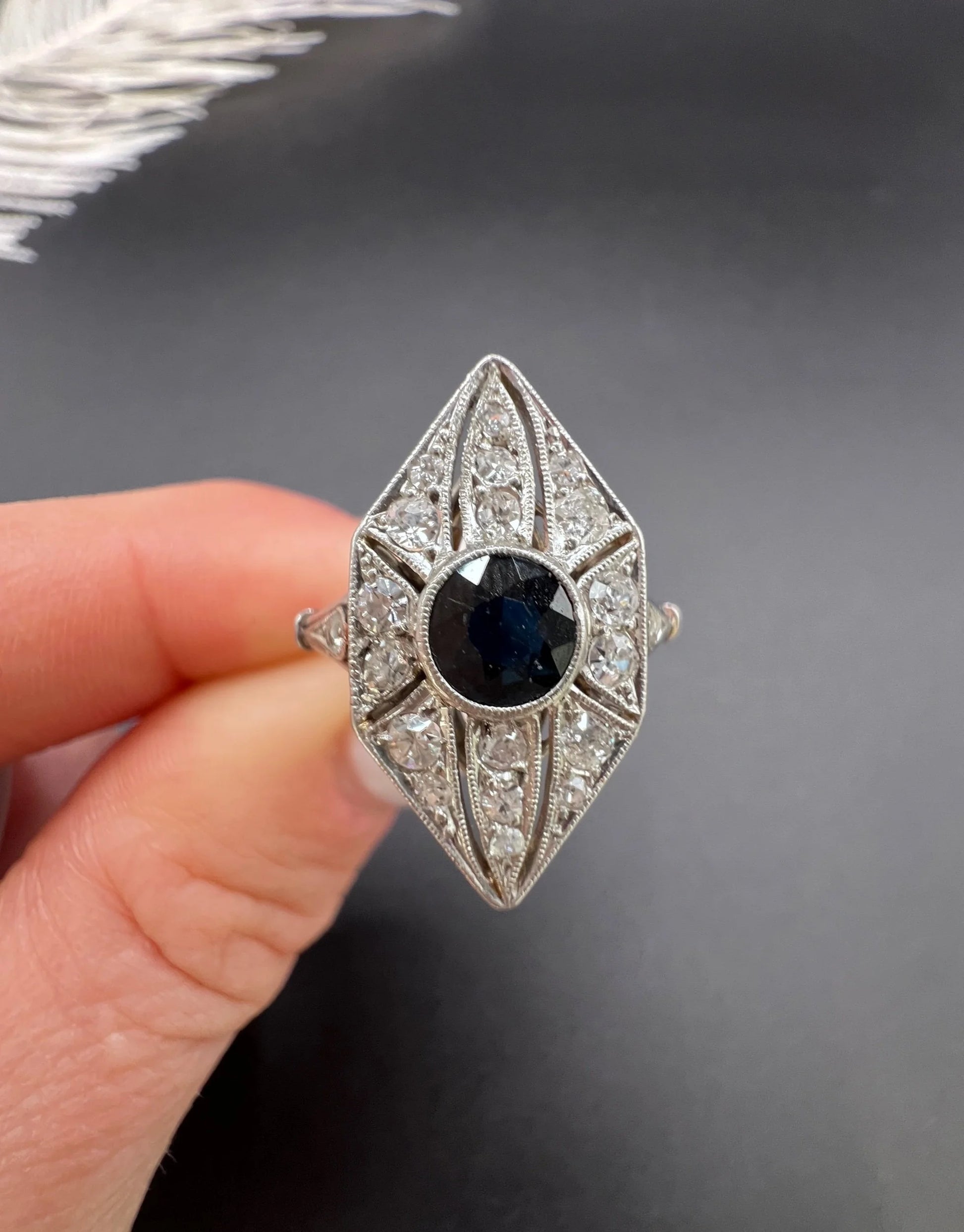 A navette shaped cluster cocktail ring with a sapphire centre surrounded by diamonds, in platinum, held in a hand