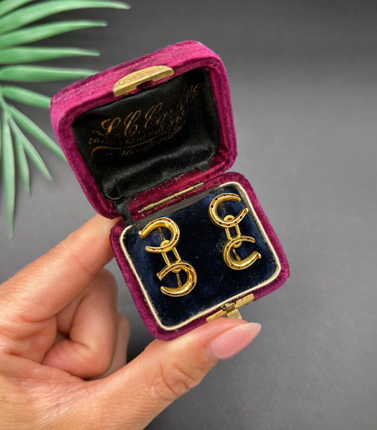 A pair of double-sided horseshoe cufflinks in yellow gold, in a vintage box, held in a hand