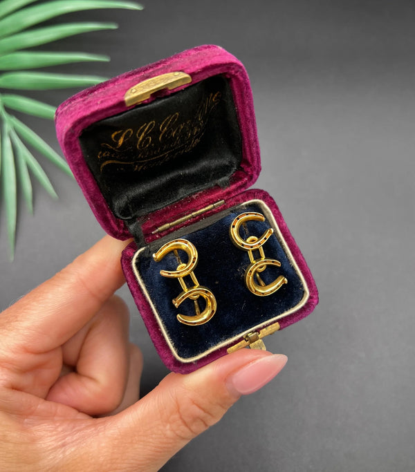A pair of double-sided horseshoe cufflinks in yellow gold, in a vintage box, held in a hand