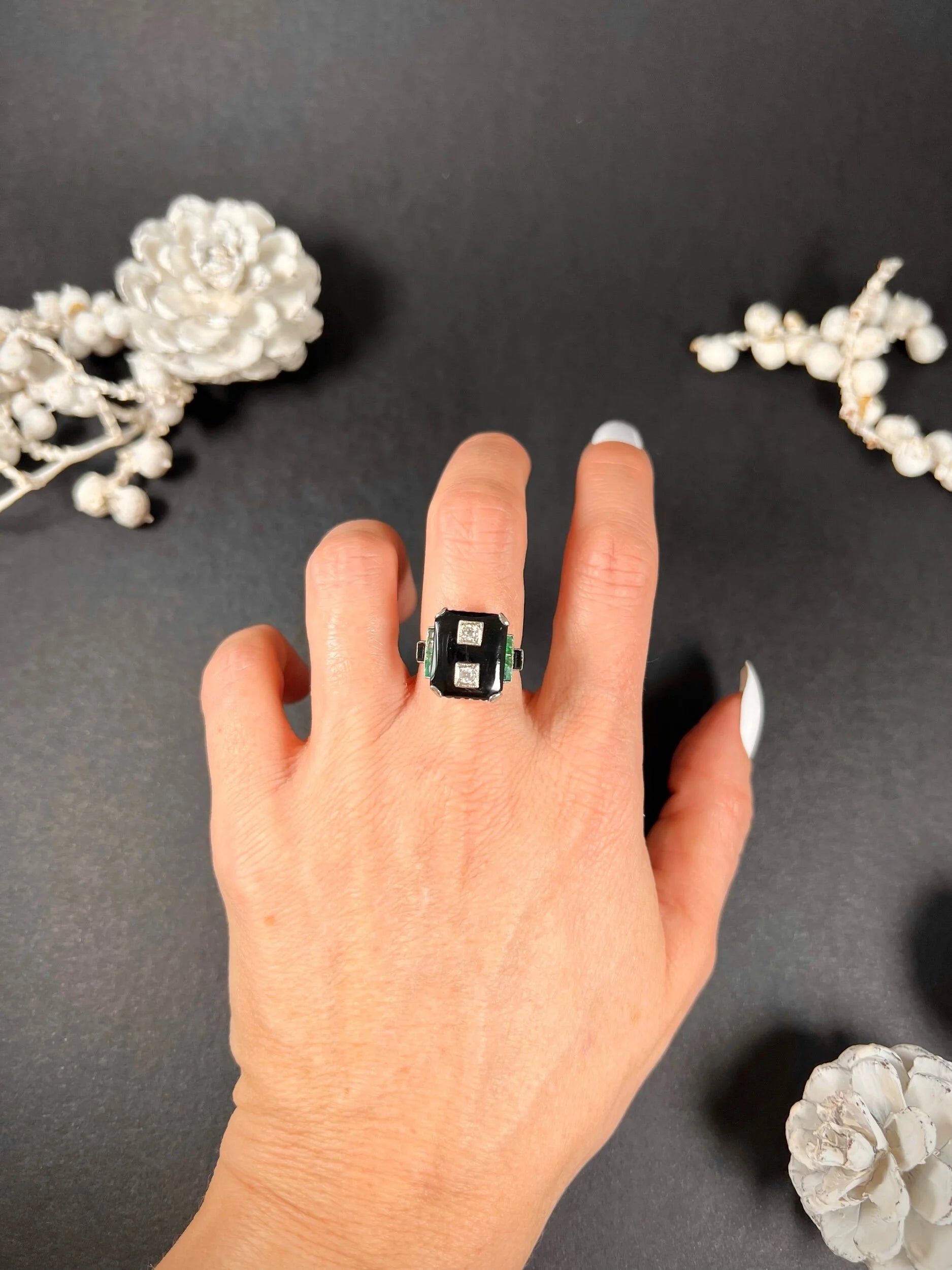 A geometric black onyx ring with diamonds and emeralds in white gold, modelled on a hand