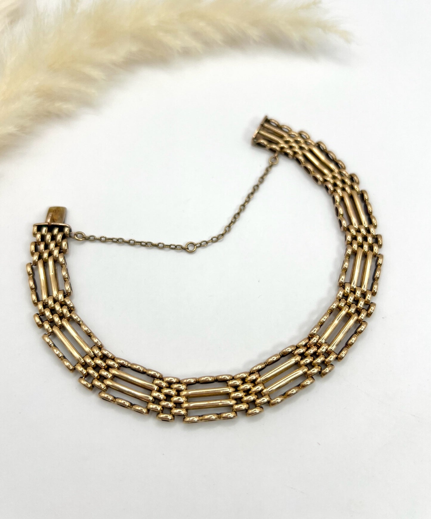 A yellow gold gate bracelet, laid flat on a white background