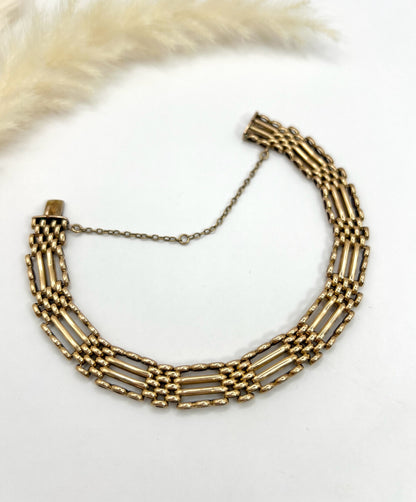 A yellow gold gate bracelet, laid flat on a white background