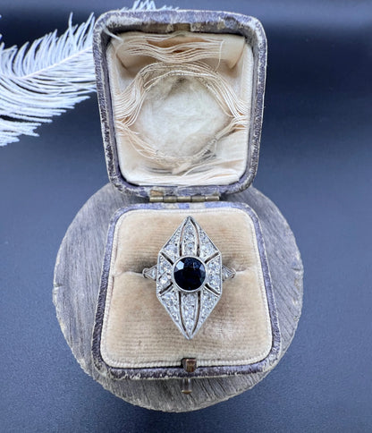 A navette shaped cluster cocktail ring with a sapphire centre surrounded by diamonds, in platinum, in an antique ring box