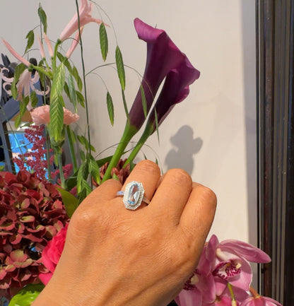 An oval blue topaz and diamond dress ring in white gold, modelled on a hand