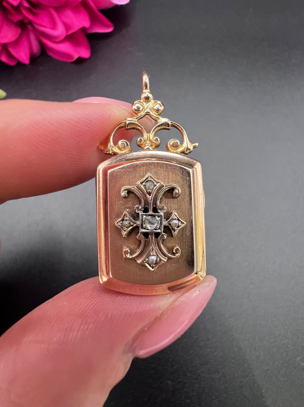 A yellow gold ornate locket with diamond fleur-de-lis detail, held in a hand
