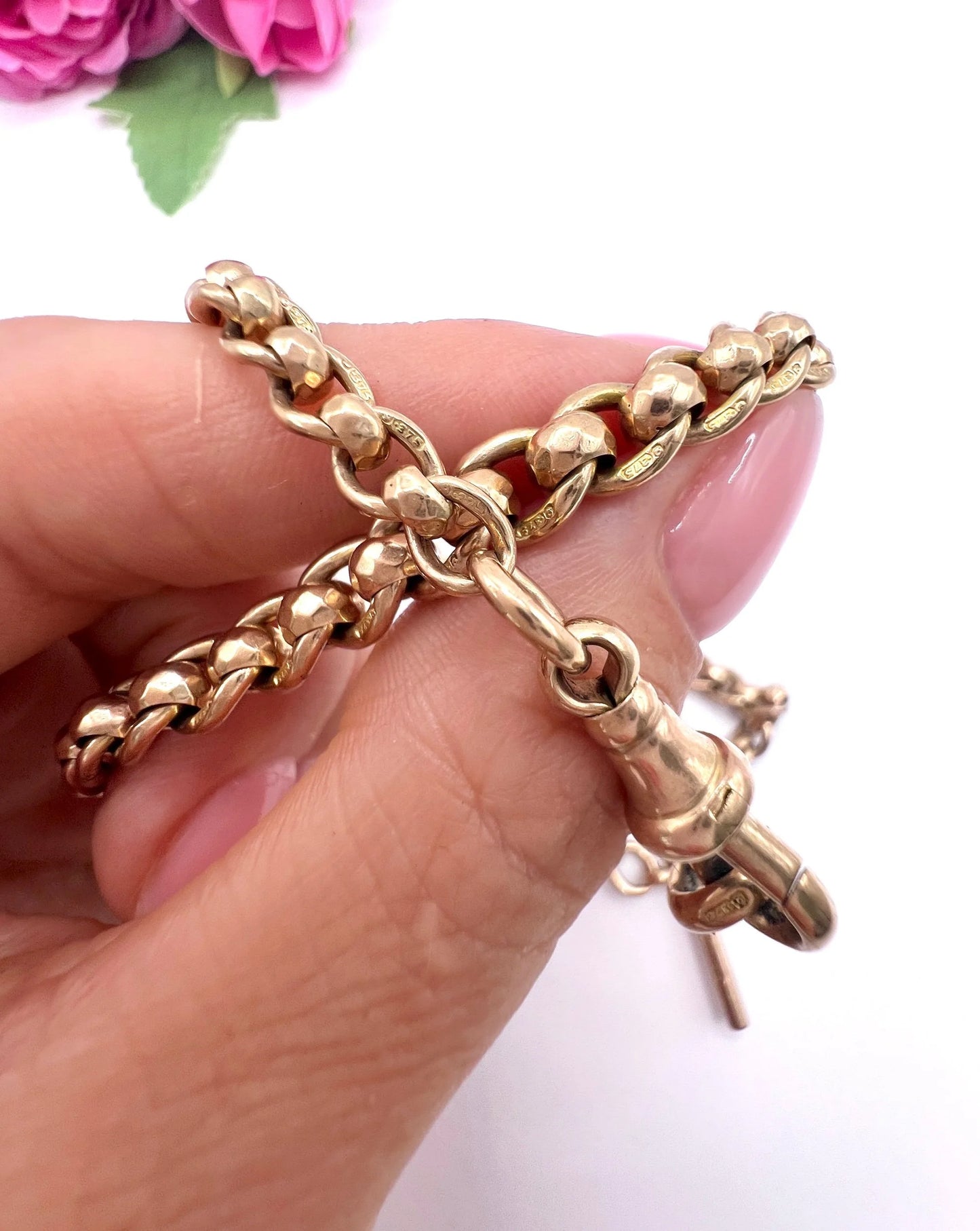 A rose gold fancy link Albert chain necklace with a T-bar attachment, held in a hand