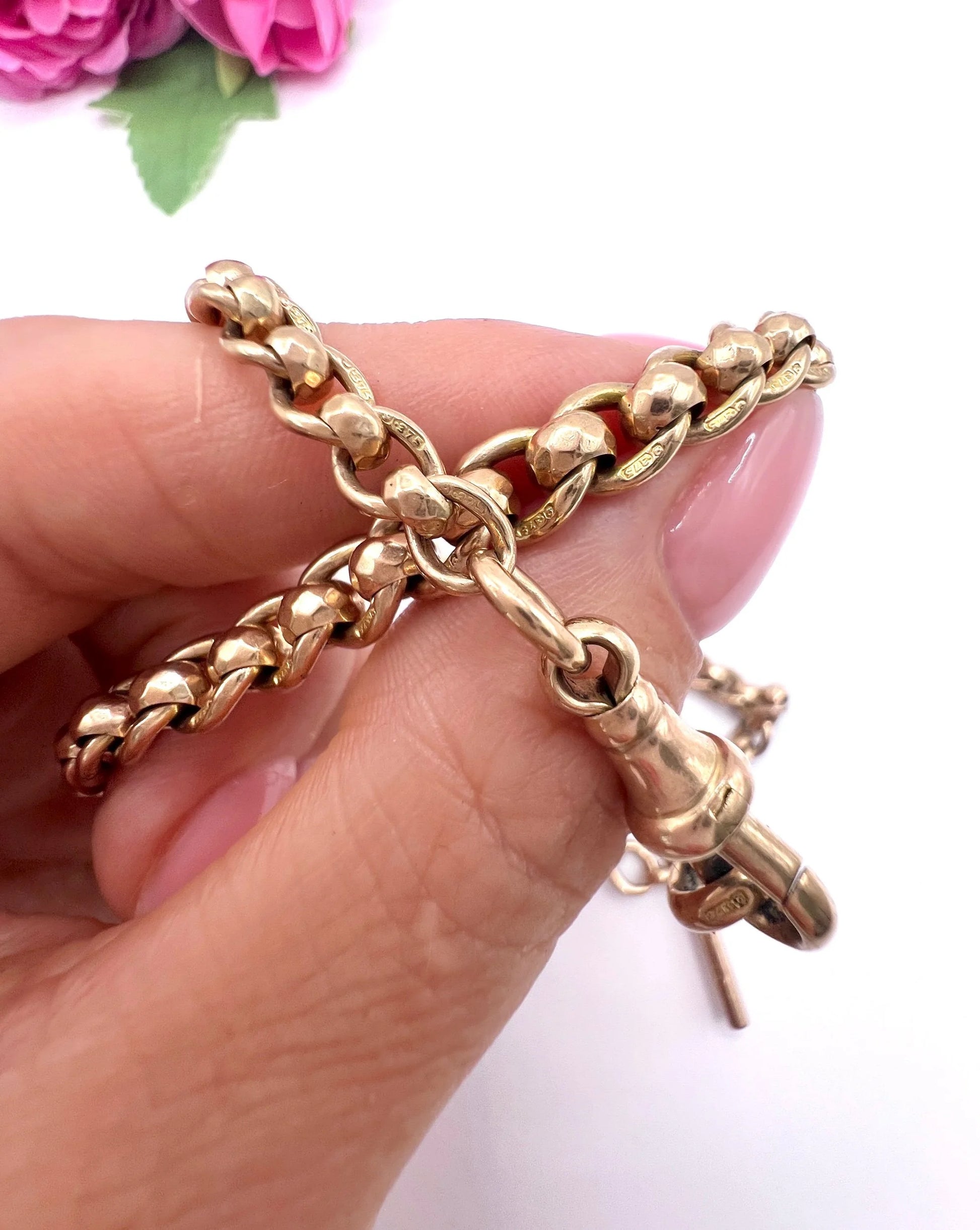 A rose gold fancy link Albert chain necklace with a T-bar attachment, held in a hand