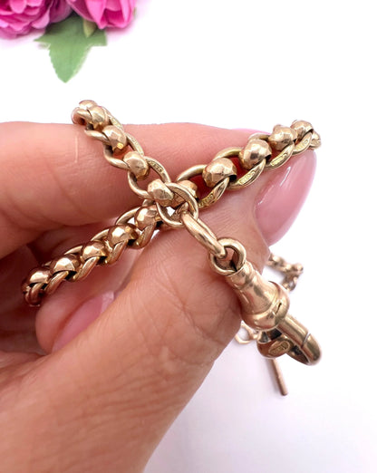 A rose gold fancy link Albert chain necklace with a T-bar attachment, held in a hand