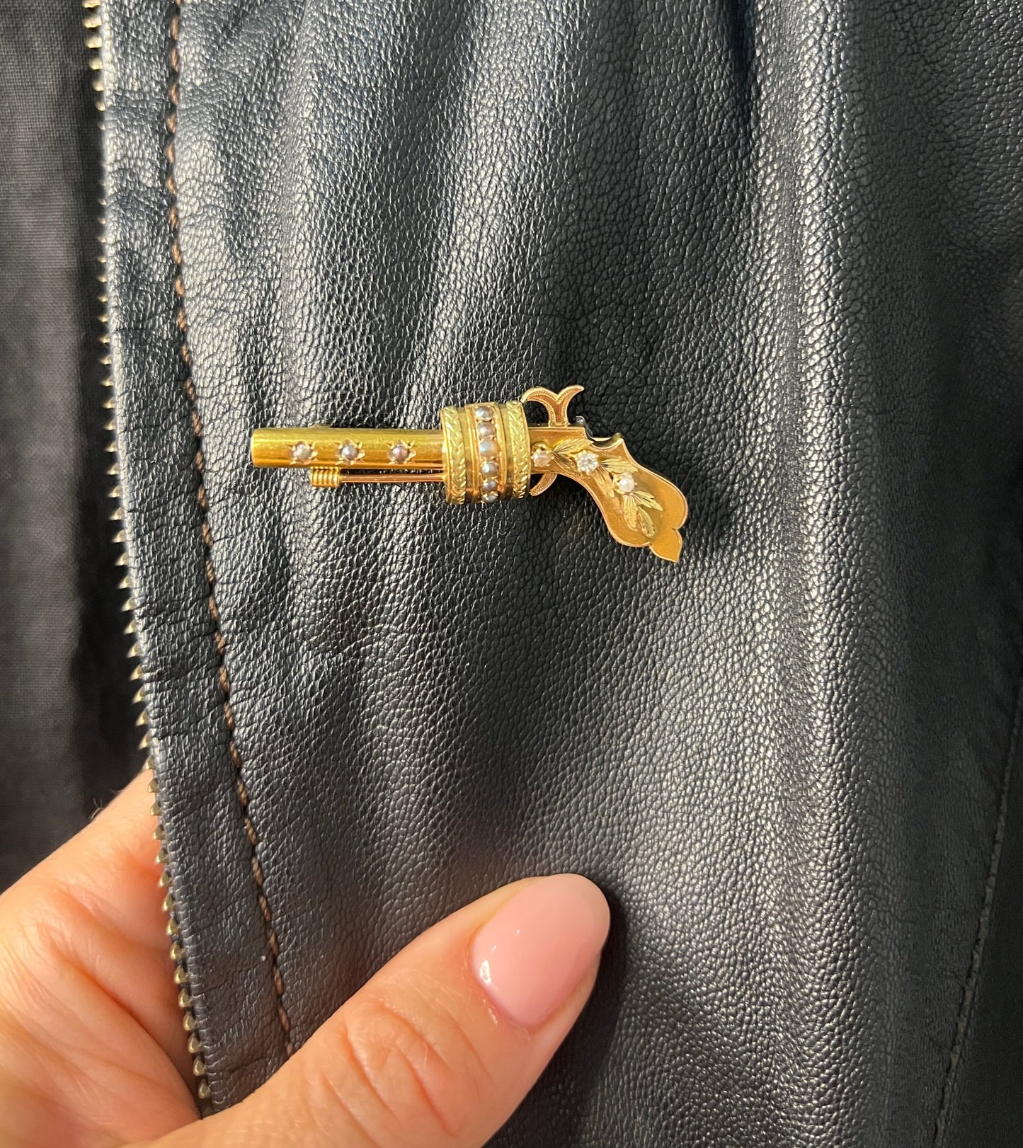 A yellow gold novelty gun brooch with diamonds and seed pearls, on a black leather jacket