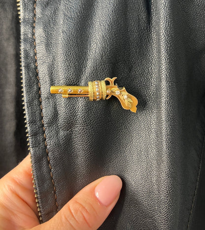 A yellow gold novelty gun brooch with diamonds and seed pearls, on a black leather jacket