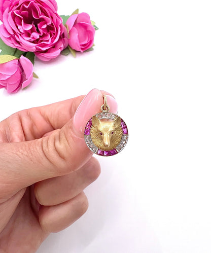 A fox head pendant in yellow gold with a ruby and diamond border, held in a hand