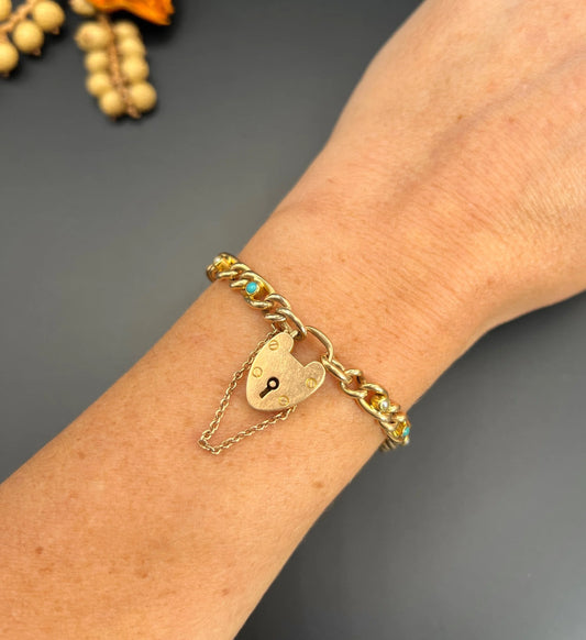 A yellow gold curb link bracelet with turquoise, pearls and a heart-shaped padlock, modelled on a wrist
