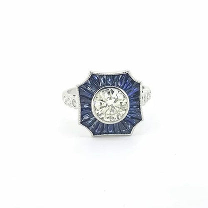 Contemporary Diamond and Sapphire Cluster Target Ring; central 1.01 carat round brilliant-cut diamond surrounded by calibre cut sapphires, three diamonds to each shoulder, in 18ct white gold.