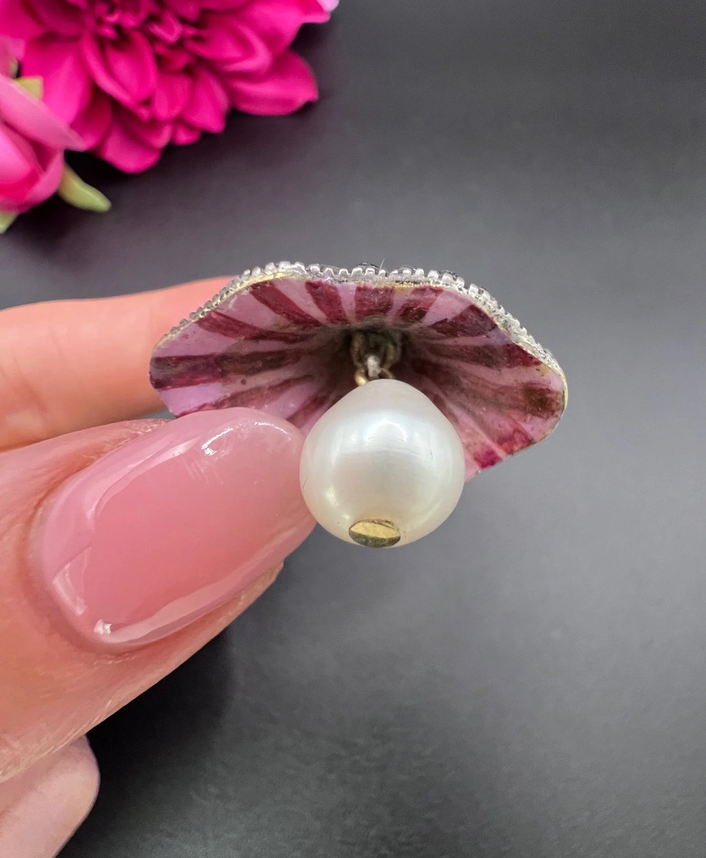 A pink enamel, diamond and pearl flower pendant in gold and silver, held in a hand