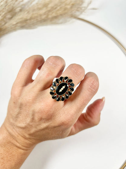 A black onyx and seed pearl fancy halo cluster ring in yellow gold, modelled on a hand