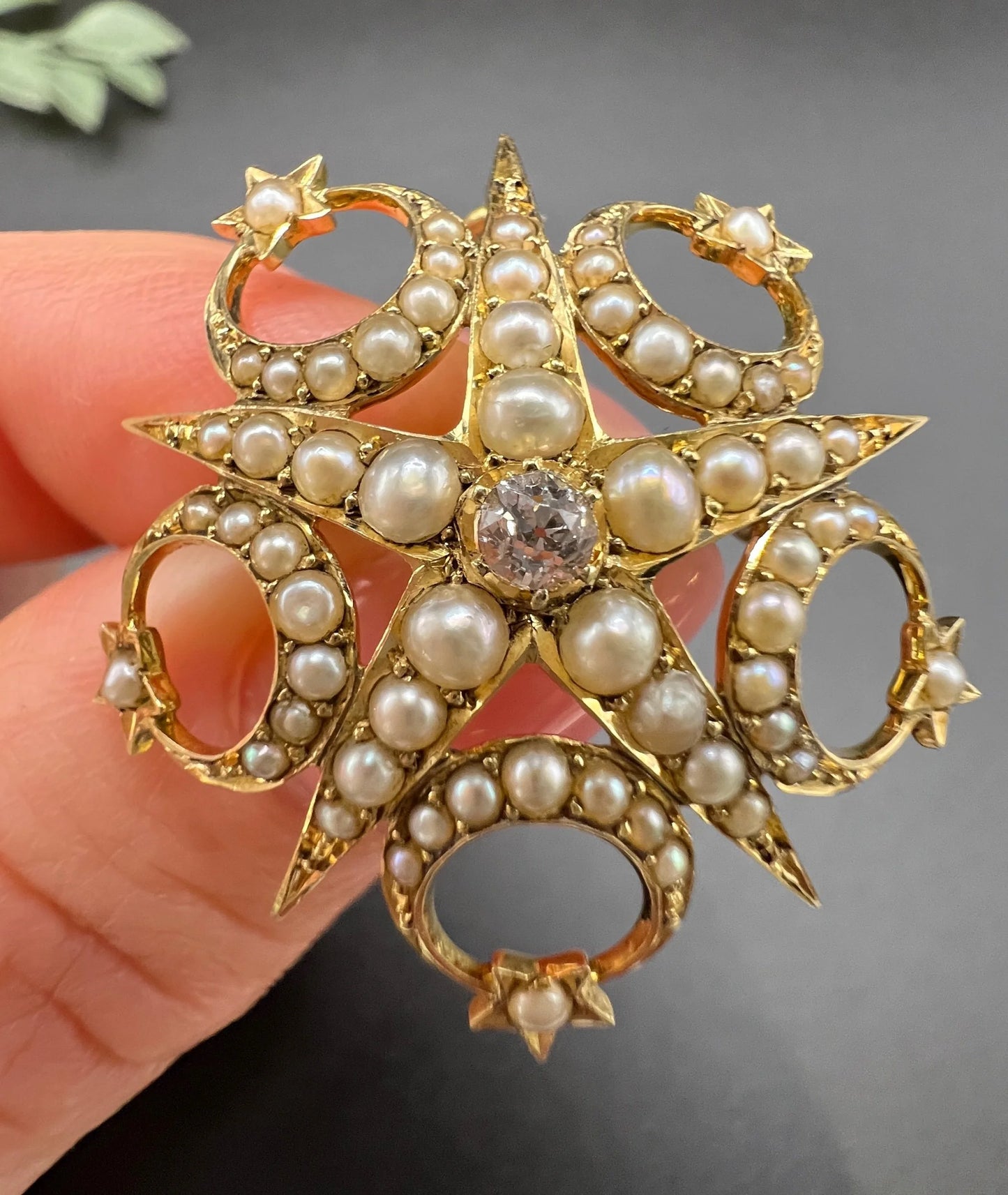 A yellow gold star and crescent brooch/pendant set with a diamond and pearls, held in a hand