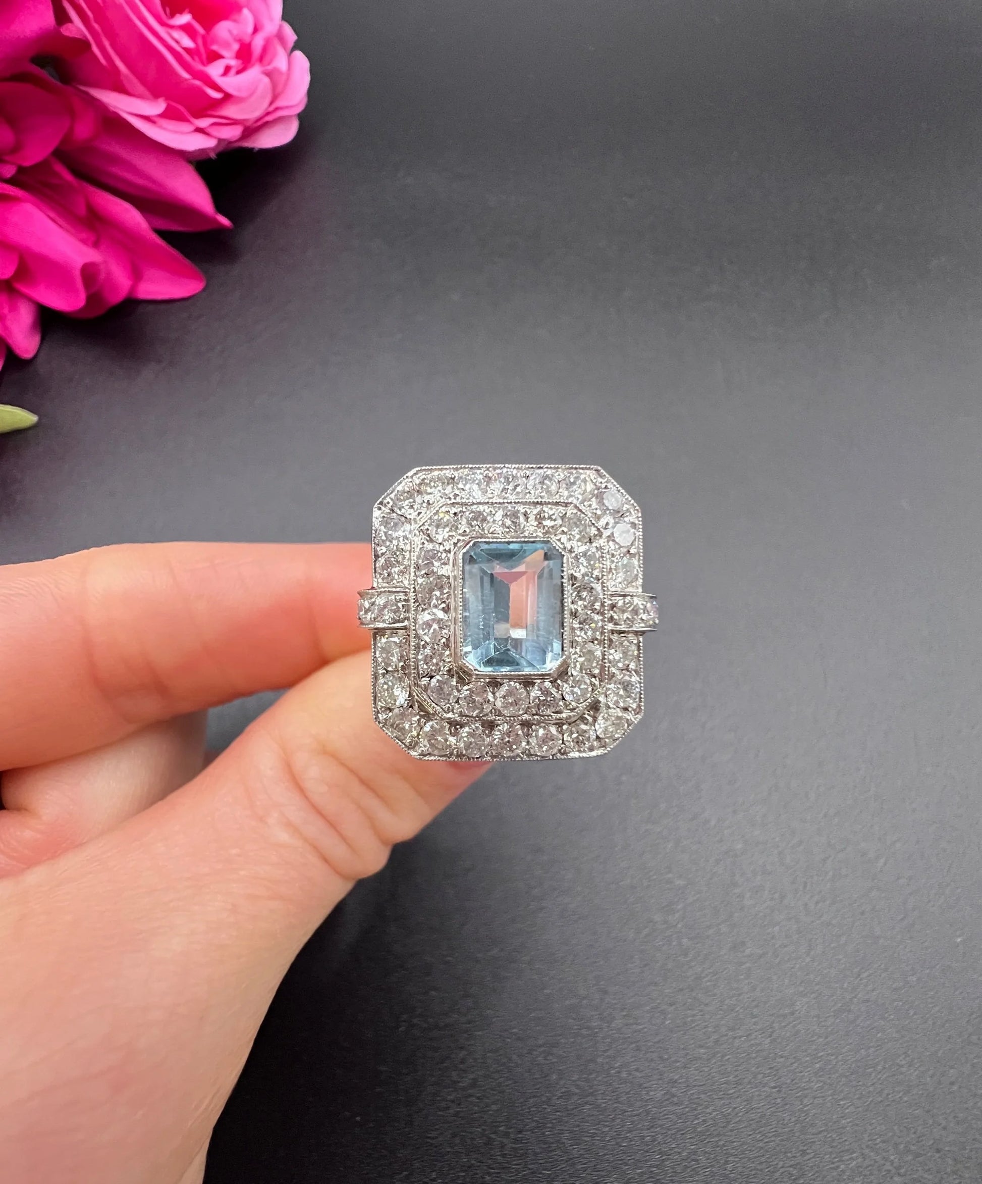 An octagonal shaped cluster ring with an aquamarine centre surrounded by two rows of diamonds, in platinum, held in a hand