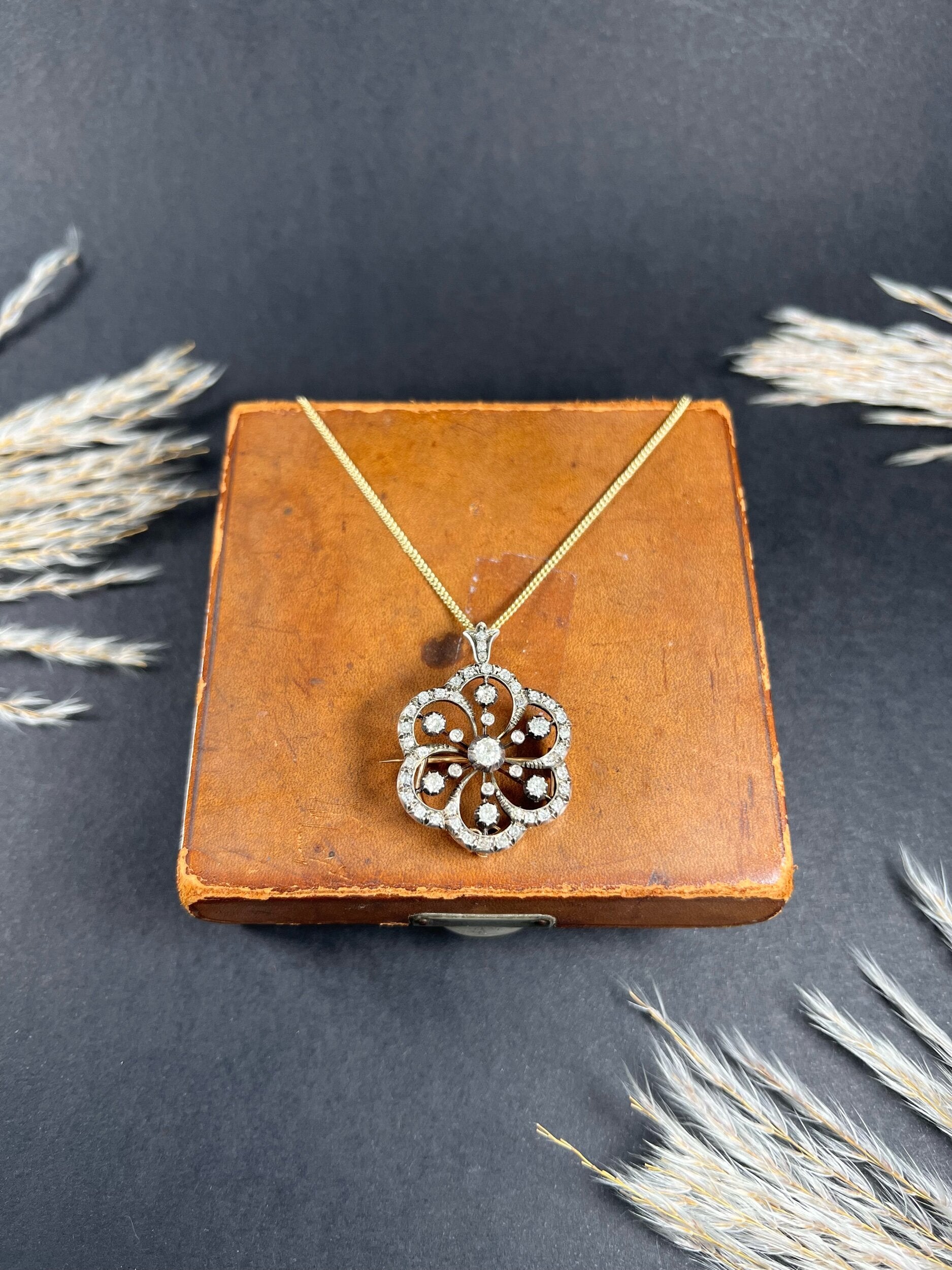 A floral design diamond set pendant/brooch on a gold chain on an antique brown jewellery box