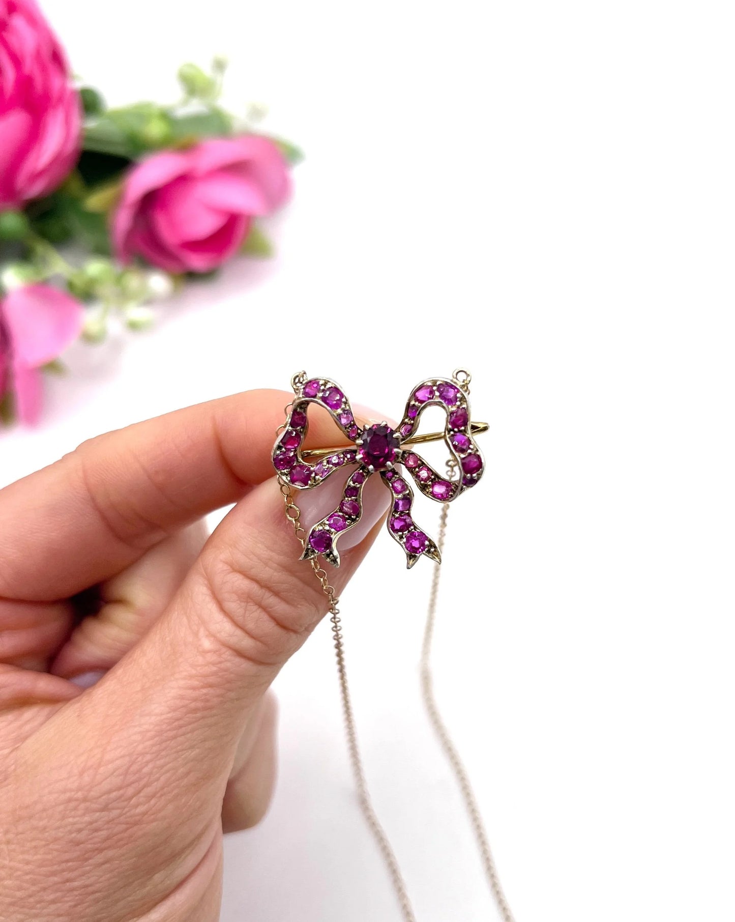 A ruby bow brooch necklace in gold and silver, held in a hand