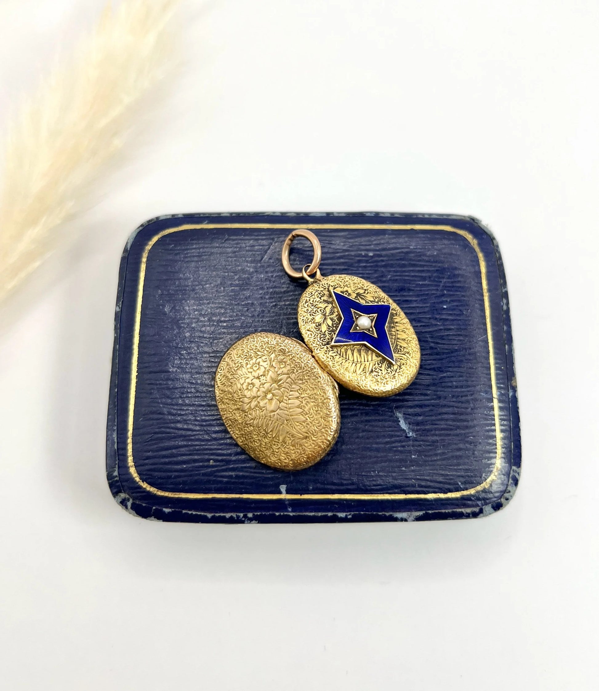 An oval yellow gold locket with a blue enamel star and seed pearl centre, open