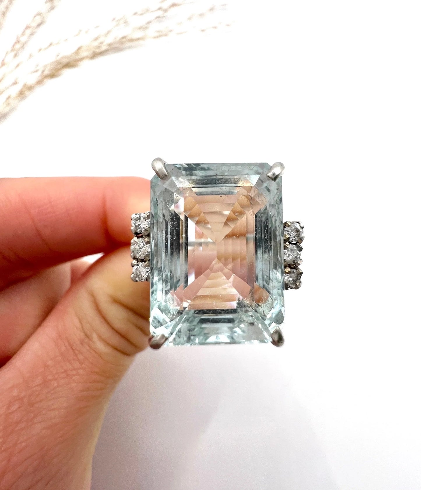 An aquamarine and diamond cocktail ring in white gold, held by a hand