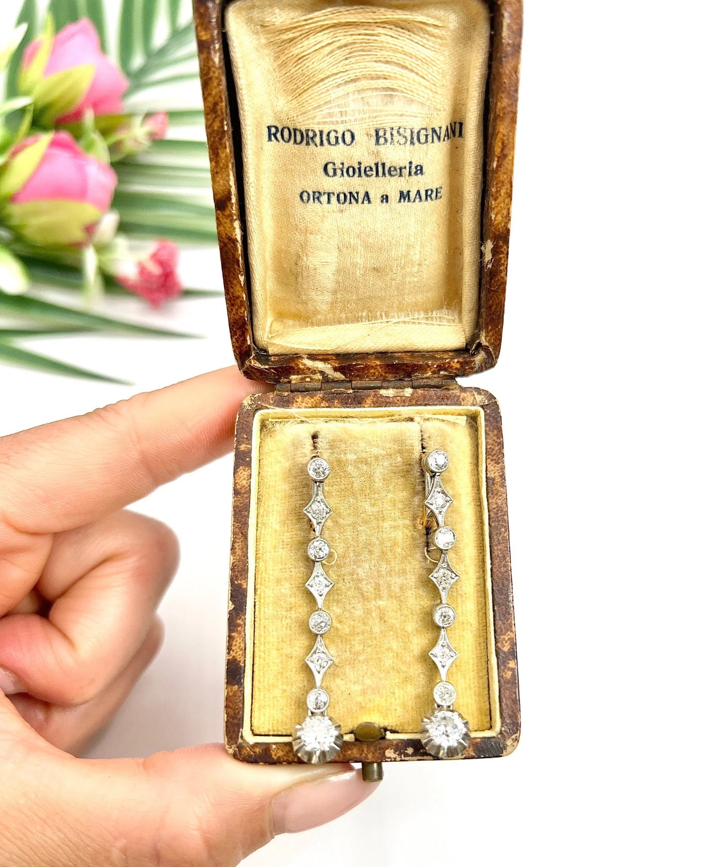 A pair of diamond drop earrings in yellow gold and platinum in an antique box, held in a hand
