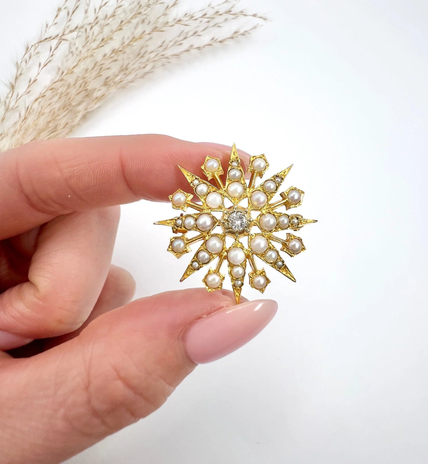 A star-shaped pearl and diamond brooch/pendant in yellow gold, held in a hand