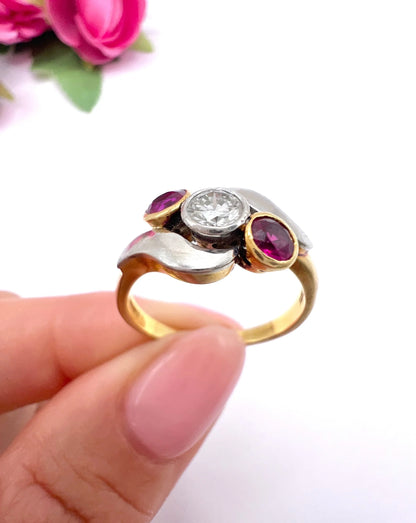 A three stone ruby and diamond crossover ring in platinum and yellow gold, held in a hand