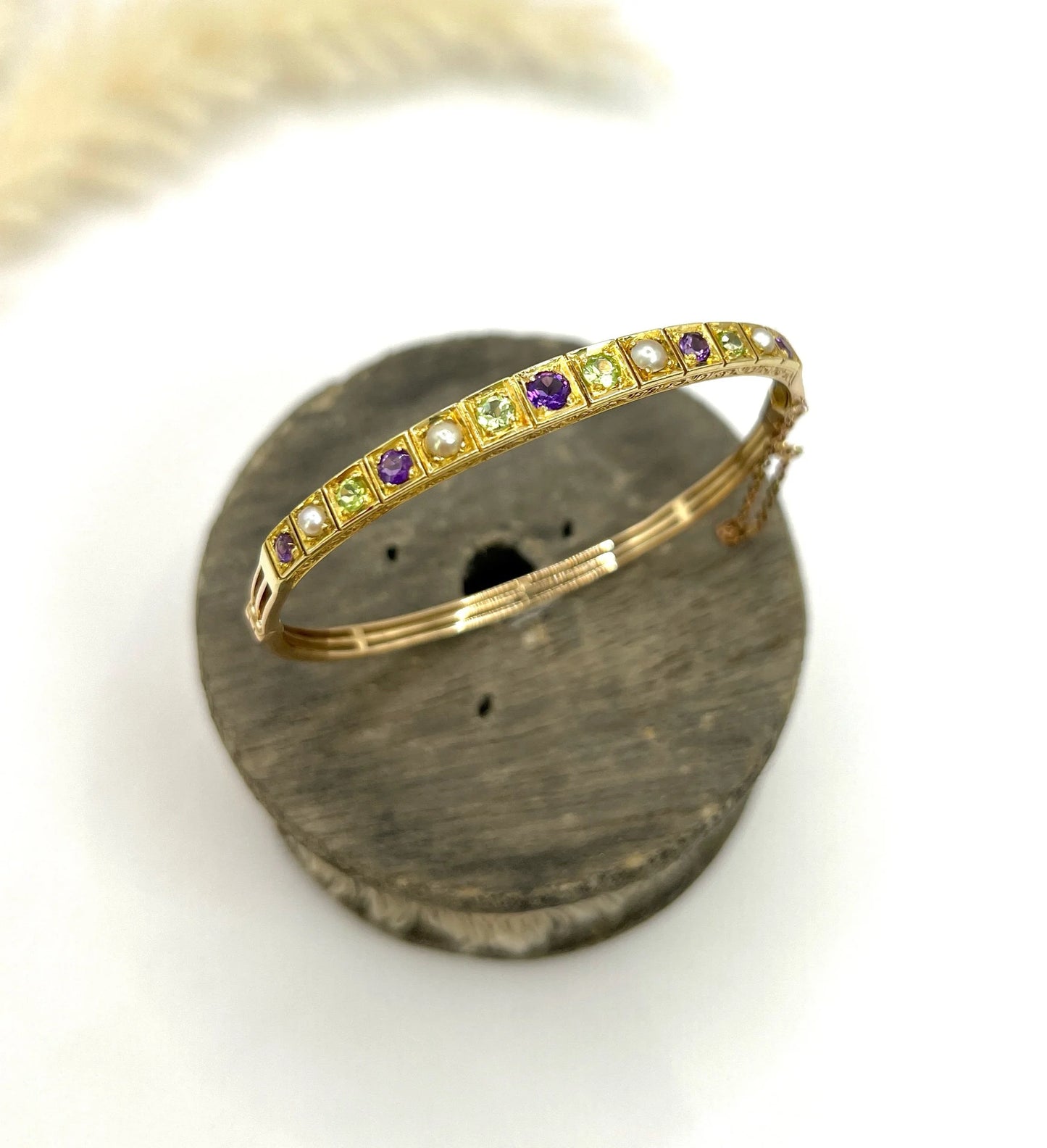 A yellow gold peridot, amethyst and pearl bangle bracelet, on a wooden spool