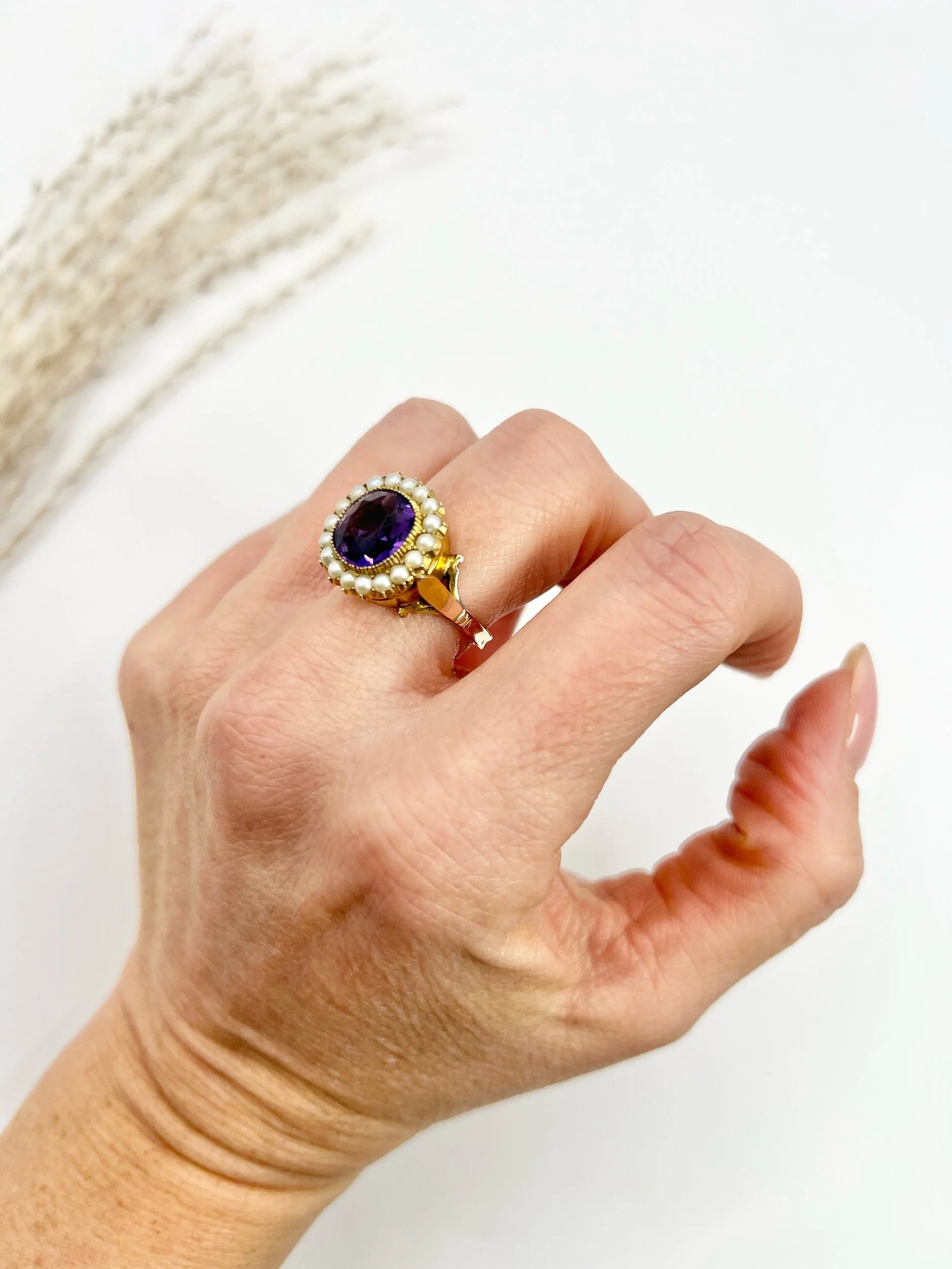 A cushion shaped amethyst cluster ring with a pearl border, in yellow gold, modelled on a hand