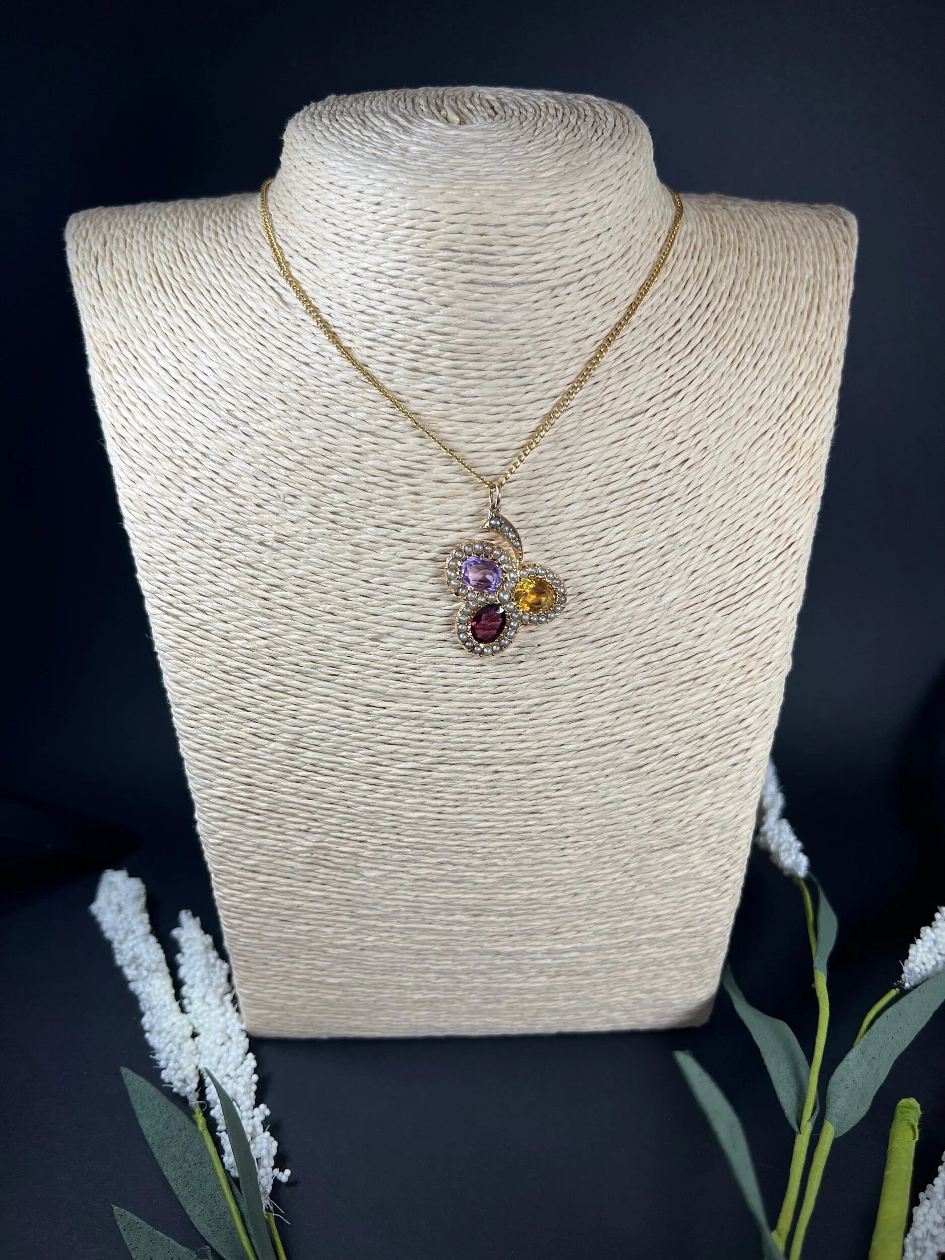 A yellow gold clover pendant with amethyst, citrine, garnet and seed pearls, with a chain, on a jewellery bust
