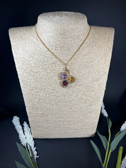A yellow gold clover pendant with amethyst, citrine, garnet and seed pearls, with a chain, on a jewellery bust
