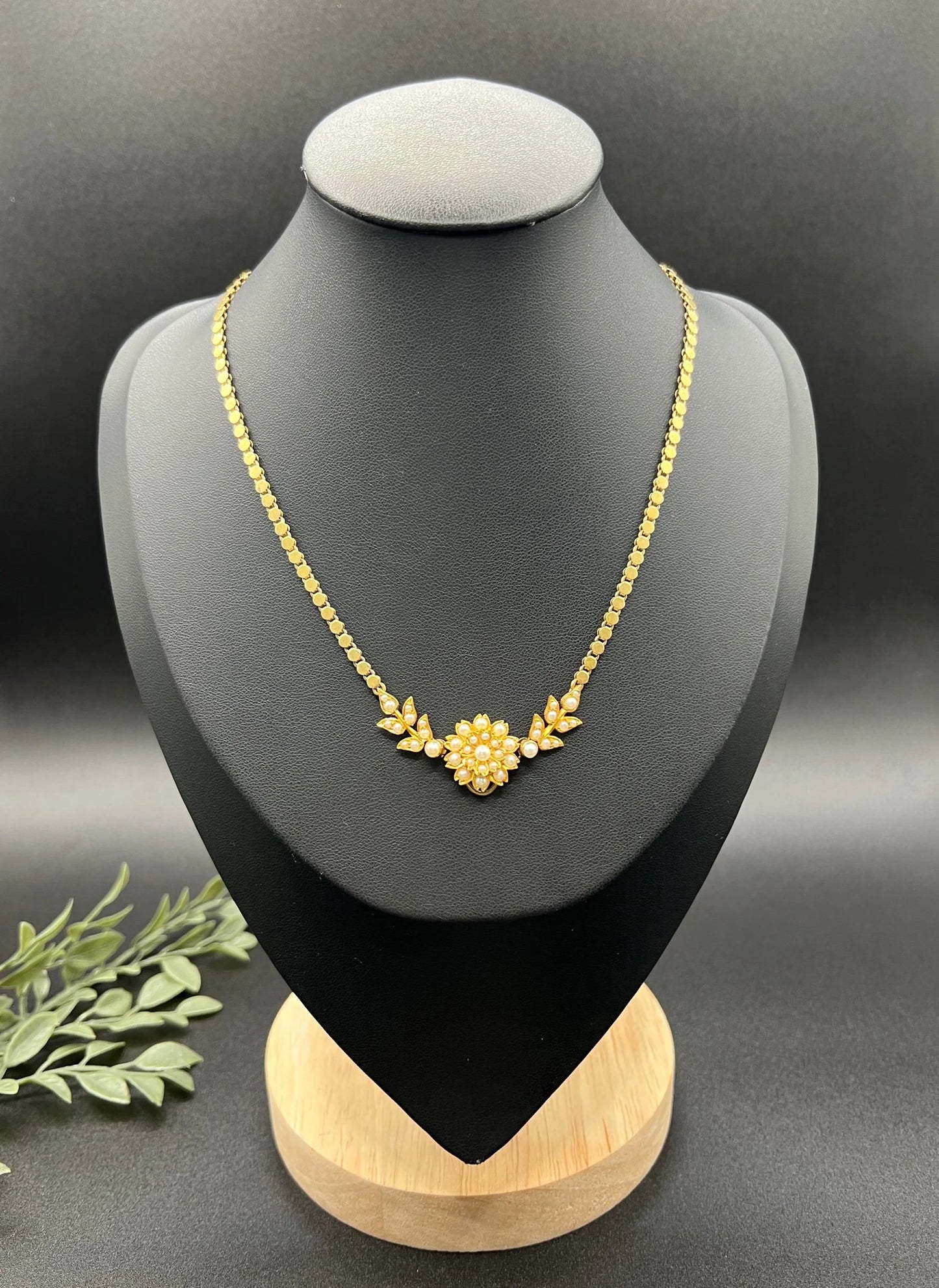 A yellow gold pearl floral necklace with integrated chain, on a black jewellery bust