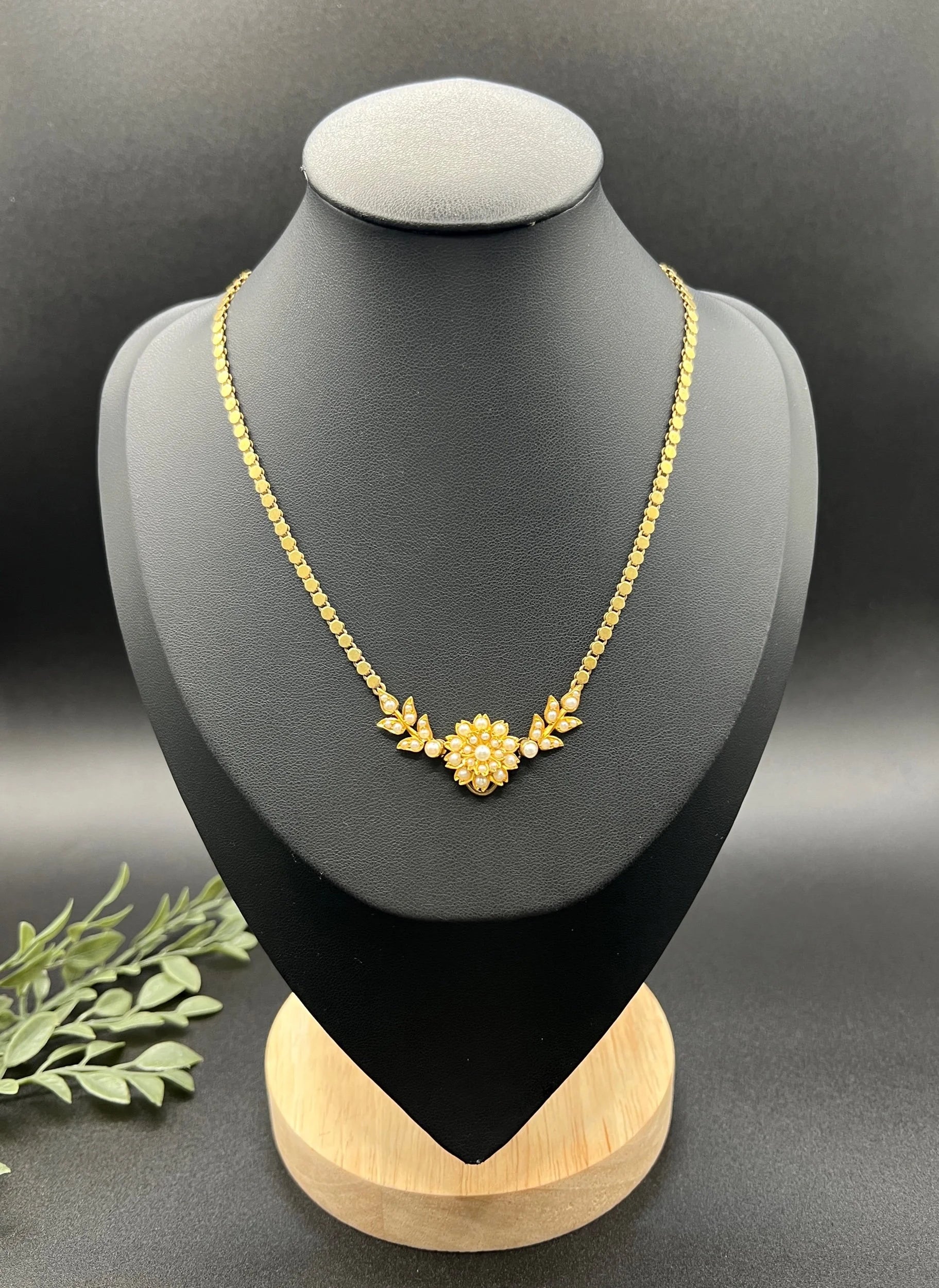 A yellow gold pearl floral necklace with integrated chain, on a black jewellery bust