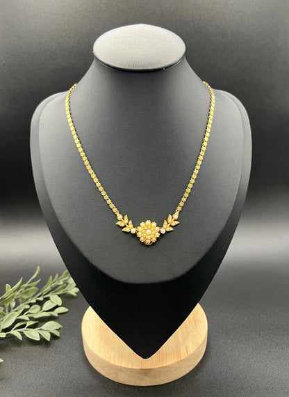 A yellow gold pearl floral necklace with integrated chain, on a black jewellery bust